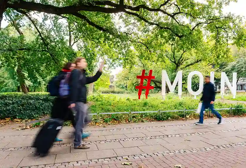 Fußgänger:innen vor dem MOIN-Schriftzug in den Wallanlagen