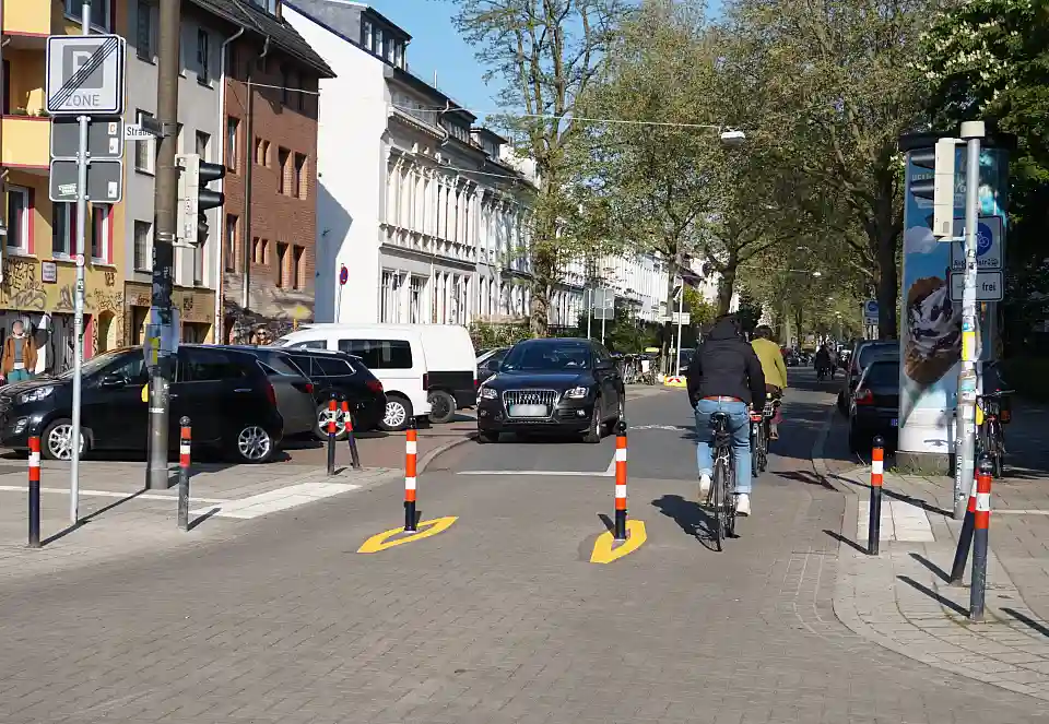 Zwei rot-wei&szlig;-gestreifte Metallpoller in der Mitte der Fahrbahn mit Radfahrenden, die hindurchfahren.