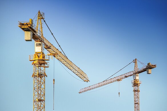 Zwei gelbe Baukräne vor blauem Himmel