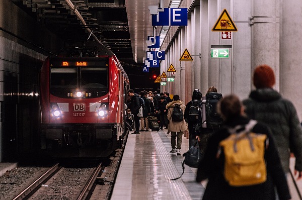 Passagiere auf Bahngleis mit wartendem Zug