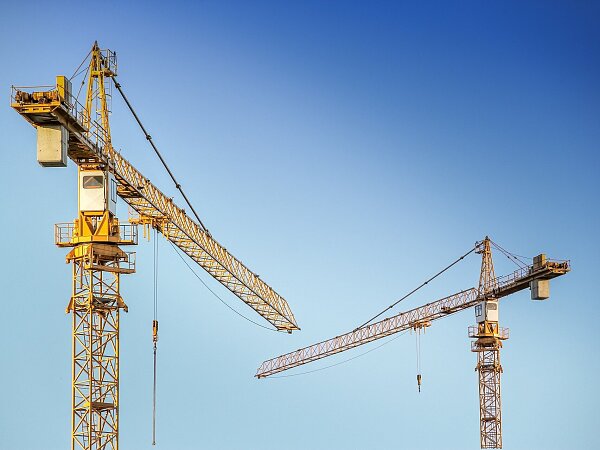 Zweigelbe Baukräne vor blauem Himmel