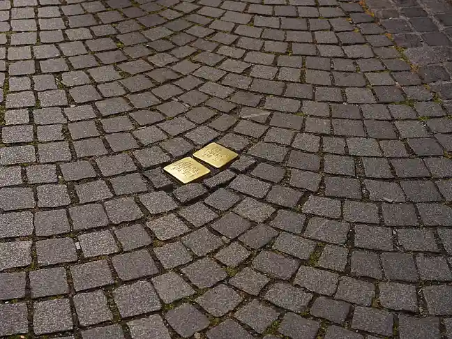 Zwei goldene Stolpersteine inmitten einer Pflasterung