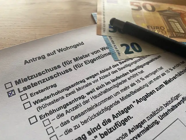Das Bild zeigt den Antrag, einen Stift und Euro-Scheine