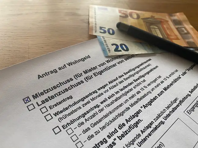 Das Bild zeigt den Antrag, einen Stift und Euro-Scheine
